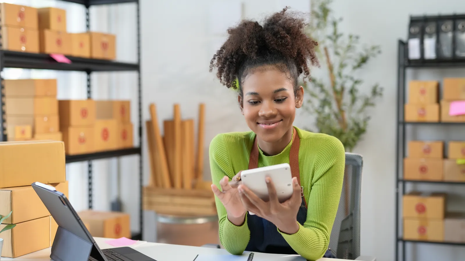 A woman calculates business finances at a bright table with a laptop