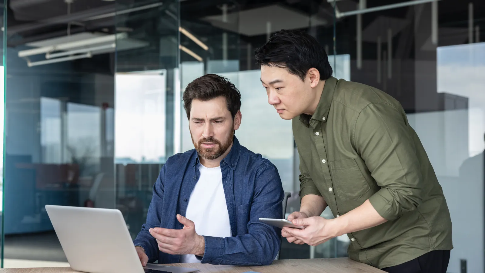 Two colleagues talk over a laptop while one holds a phone